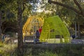 A family playing on the playground with a yellow jungle gym at Tongva Park with brown fallen leaves and lush green trees, plants