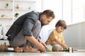 Family playtime. Happy interested father playing with little son, riding wooden toy train on railway, sitting on floor Royalty Free Stock Photo