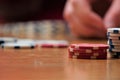 Close up of poker chips on wood table with bokeh hand