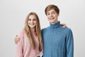 Family portrait of brother and sister against gray background. Young hipster fair-haired man dressed in blue sweater Royalty Free Stock Photo