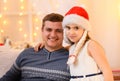 Family portrait - father and daughter in home interior decorated with holiday lights and gifts, dressed in santa hat for new year