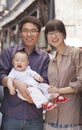 Family portrait, father is holding the baby, looking at camera, outdoors