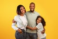 Family portrait. Happy african american parents and cute daughter embracing and posing over yellow background Royalty Free Stock Photo