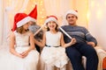 Family portrait - parent and children in home interior decorated with holiday lights and gifts, dressed in santa hat for new year