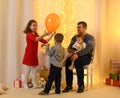 Family portrait - parent and children play in home interior decorated with holiday lights and gifts