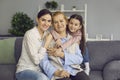 Family portrait of smiling women of three generations sitting on sofa in living room. Royalty Free Stock Photo