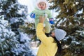 Family portrait in the winter forest, mother lift the baby up in her arms, bright snowy fir trees, beautiful nature