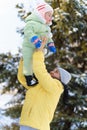 Family portrait in the winter forest, mother lift the baby up in her arms, bright snowy fir trees, beautiful nature