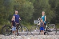 Family portrait of young happy mother, father and two cute blond children, boy and girl standing at bicycles on pebbled river bank Royalty Free Stock Photo