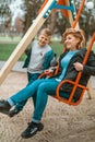 Family portrait young pretty happy mother and teenager son having fun on a swing in city park