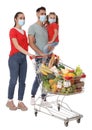 Family with protective masks and shopping cart full of groceries on white background Royalty Free Stock Photo