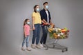 Family with protective masks and shopping cart full of groceries on light grey background Royalty Free Stock Photo