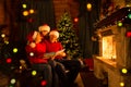 Family read Christmas book sitting on coach in front of fireplace in festive decorated house interior