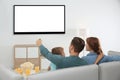 Family with remote control sitting on couch and watching TV at home, space for design on screen Royalty Free Stock Photo