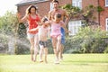 Family Running Through Garden Sprinkler