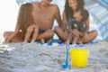 Family, sand and relax on beach with bucket, spade and umbrella for playing by ocean coast. Blue and yellow toy on sandy
