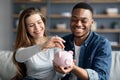 Family Savings. Young Interracial Couple Putting Coin In Piggybank At Home Royalty Free Stock Photo