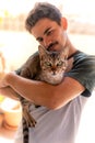 Vertical photo. Young man hugs a green-eyed tabby cat. The cat looks at the camera. Royalty Free Stock Photo