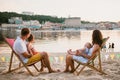 Family at seaside in evening open-air cafe. Mother and father and two sons sit on sun loungers, looking at sunset on sandy beach Royalty Free Stock Photo