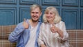 Family of senior gray-haired mother and handsome adult son or grandson showing thumbs up gesture