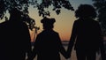 Family silhouette holding hands walking together at sunset river bridge closeup. Royalty Free Stock Photo