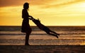 Family, silhouette and sunset at beach with mother swinging child against yellow sky with love, care and support on Royalty Free Stock Photo