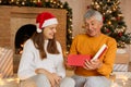Family sitting with their grandfather celebrating Christmas in cozy house, woman in santa claus hat giving new year present, happy Royalty Free Stock Photo