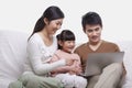 Family smiling and sitting together on the sofa looking at laptop, studio shot Royalty Free Stock Photo