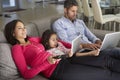 Family On Sofa With Laptop And Digital Tablet Watching TV