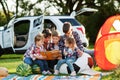 Family spending time together. Mother reading book outdoor with kids against their suv car Royalty Free Stock Photo