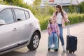 Family standing by the car with suitcases and waiting journey. Little girl sitting on kid suitcase.