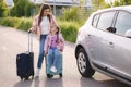 Family standing by the car with suitcases and waiting journey. Little girl sitting on kid suitcase.