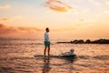 Family summer vacations. Father and daughter surfing on a sup board. Sunset sky and sea of peach color at the background Royalty Free Stock Photo