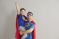 Family in superhero costumes. Father holds his son in his arms standing on a gray background. Royalty Free Stock Photo