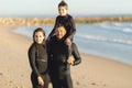 A family of surfers stands on the seashore in wetsuits
