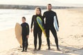 A family of surfers in wetsuits standing on the seashore holding surfboards Royalty Free Stock Photo