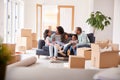 Family Taking A Break And Sitting On Sofa Celebrating Moving Into New Home Together