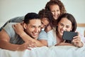 Family taking a selfie with a cellphone in bed. Happy hispanic family taking photos in bed on a smartphone. Parents