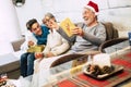 Family with teenager and grandfathers sitted at the sofa at home the morning of christmas laughing and openening their presents