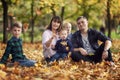 A family with three children are sitting in an autumn park among fallen yellow leaves. Love and tenderness. Camping. Soft focus Royalty Free Stock Photo