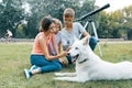 Family of three children are walking in the park with white dog Husky, sitting on the lawn, having fun looking at mobile phone Royalty Free Stock Photo