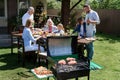 Family of three generations eating and drinking at table while grilling meat outdoors Royalty Free Stock Photo