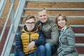 Family of three hugging people sitting on metal stairs at brick building background Royalty Free Stock Photo