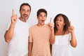 Family of three, mother, father and son standing over white isolated background pointing finger up with successful idea