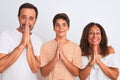 Family of three, mother, father and son standing over white isolated background praying with hands together asking for forgiveness Royalty Free Stock Photo
