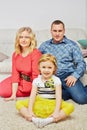 Family of three sits on carpet in light room,