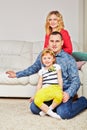 Family of three sits on carpet and on soft in
