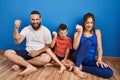 Family of three sitting on the floor at home angry and mad raising fist frustrated and furious while shouting with anger