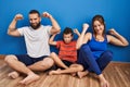 Family of three sitting on the floor at home showing arms muscles smiling proud