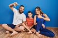 Family of three sitting on the floor at home smiling making frame with hands and fingers with happy face Royalty Free Stock Photo